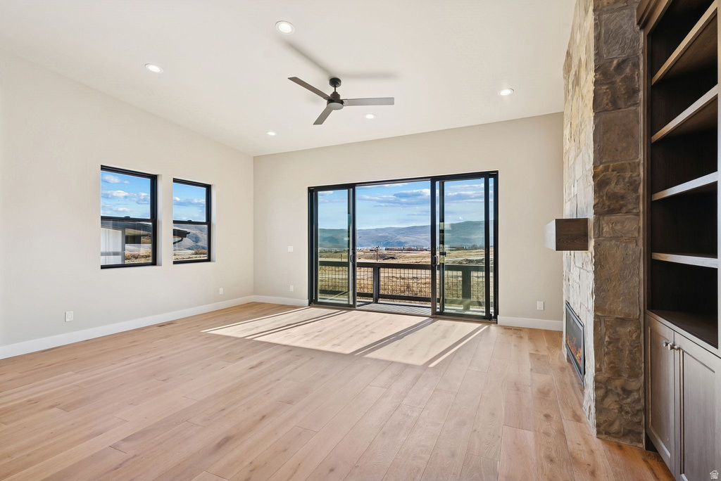 Bright interior featuring a stone-clad fireplace with built-in shelving, wood-finish flooring, and a ceiling fan