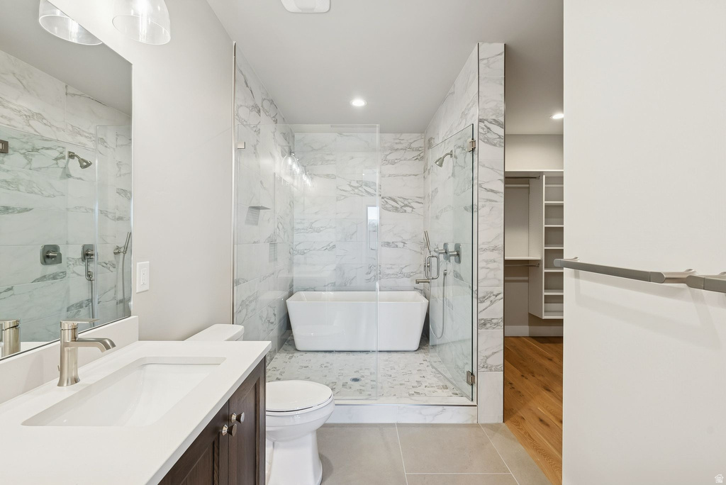 Bathroom featuring a freestanding soaking tub within a glass-enclosed shower, marble-finish wall tiling, and a vanity with an integrated sink and brushed nickel faucet
