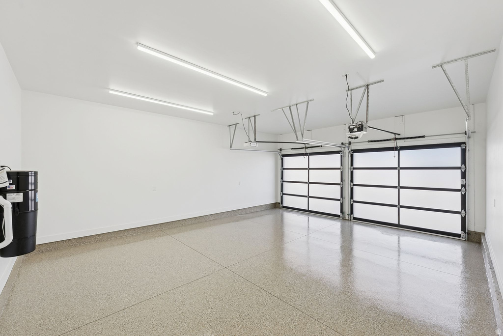 Spacious two-car garage featuring a speckled epoxy floor coating, two contemporary glass panel garage doors, and ample overhead lighting
