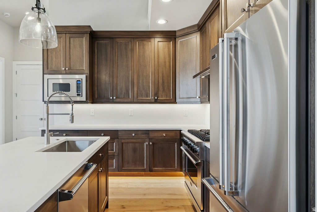 Gourmet kitchen featuring dark wood cabinetry, stainless steel appliances, white countertops, a large island with an undermount sink, and wood-finish flooring