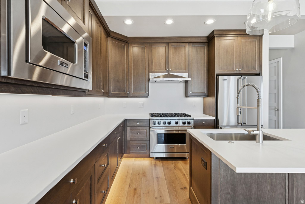 Contemporary kitchen featuring wood cabinetry, stainless steel appliances, light-toned countertops, and wood-finish flooring