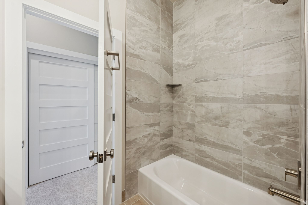Contemporary bathroom featuring a white porcelain tub and shower combination with light gray tiled walls, brushed nickel fixtures, and a recessed corner shelf