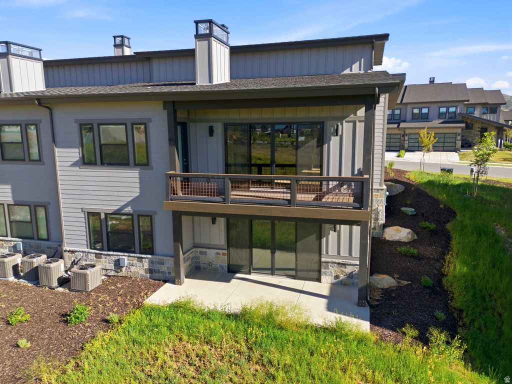 Multi-level exterior featuring a covered deck with a dark railing system, a ground-level patio, and a stone-clad foundation
