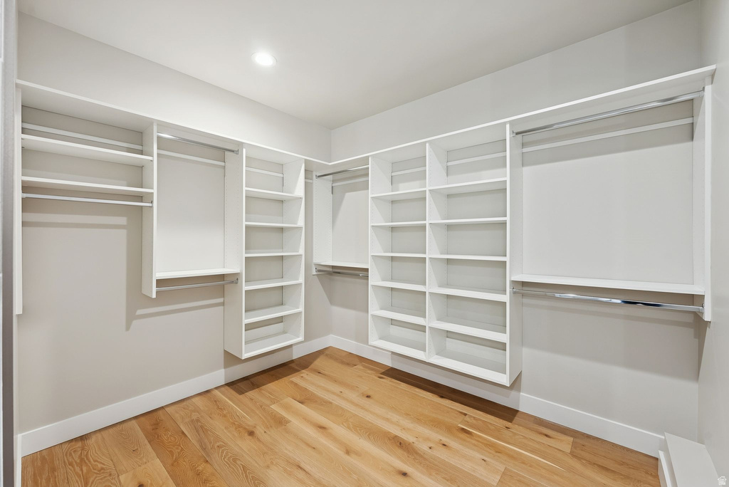 Spacious walk-in closet featuring extensive built-in shelving, multiple hanging rods, recessed ceiling lighting, and wood-finish flooring