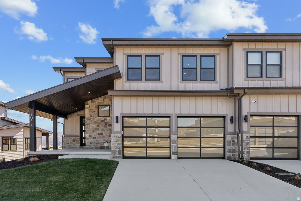Modern multi-story exterior featuring a stone facade, vertical siding, and a prominent covered entryway with recessed lighting