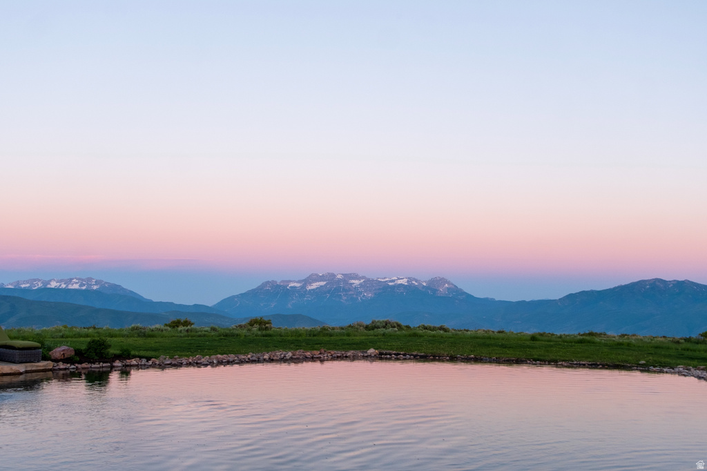 Reflecting pool with a stone edge, expansive green lawn, and distant snow-capped mountains