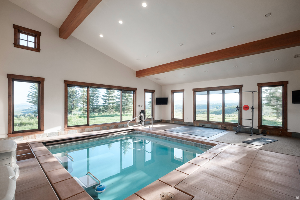 Indoor swimming pool featuring a tiled surround and natural light from multiple windows