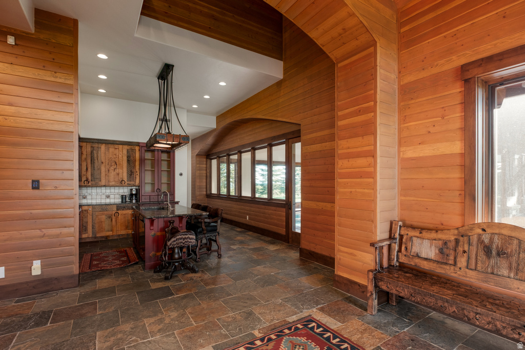 Expansive interior featuring rich wood paneling, slate tile flooring, a functional kitchen island with seating, a built-in wet bar, and multiple large windows