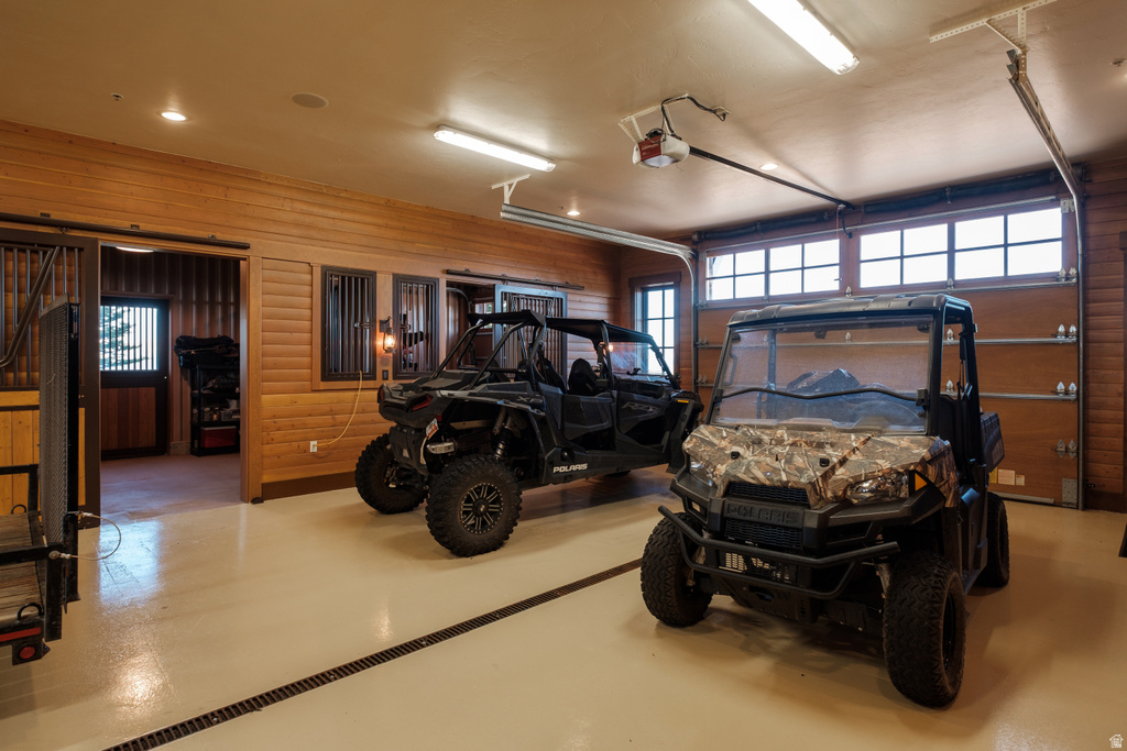 Spacious garage featuring light-toned flooring with a drainage system, wood-finish paneling, and track lighting