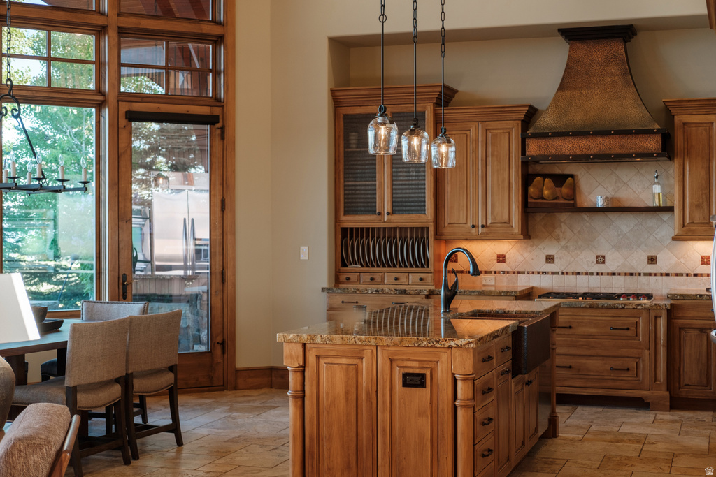 Gourmet kitchen featuring a central island with a farmhouse sink, pendant lighting, custom wood cabinetry, and a textured metal range hood