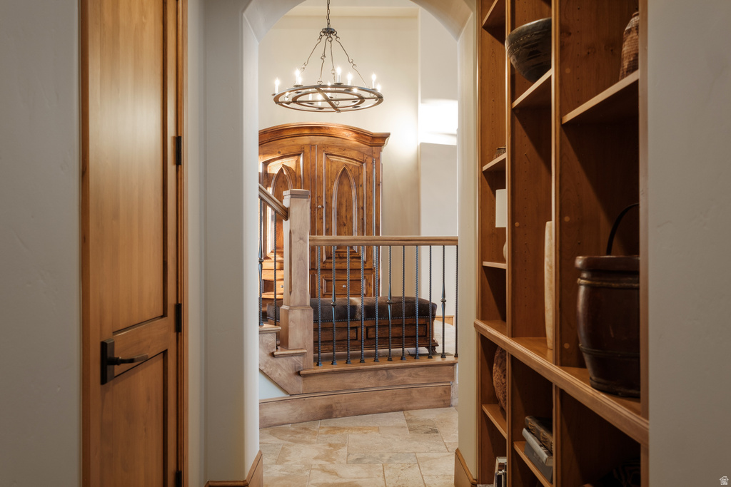 Arched entryway featuring an iron chandelier, built-in wooden shelving, natural wood doors, a wood staircase with iron balusters, and tiled flooring