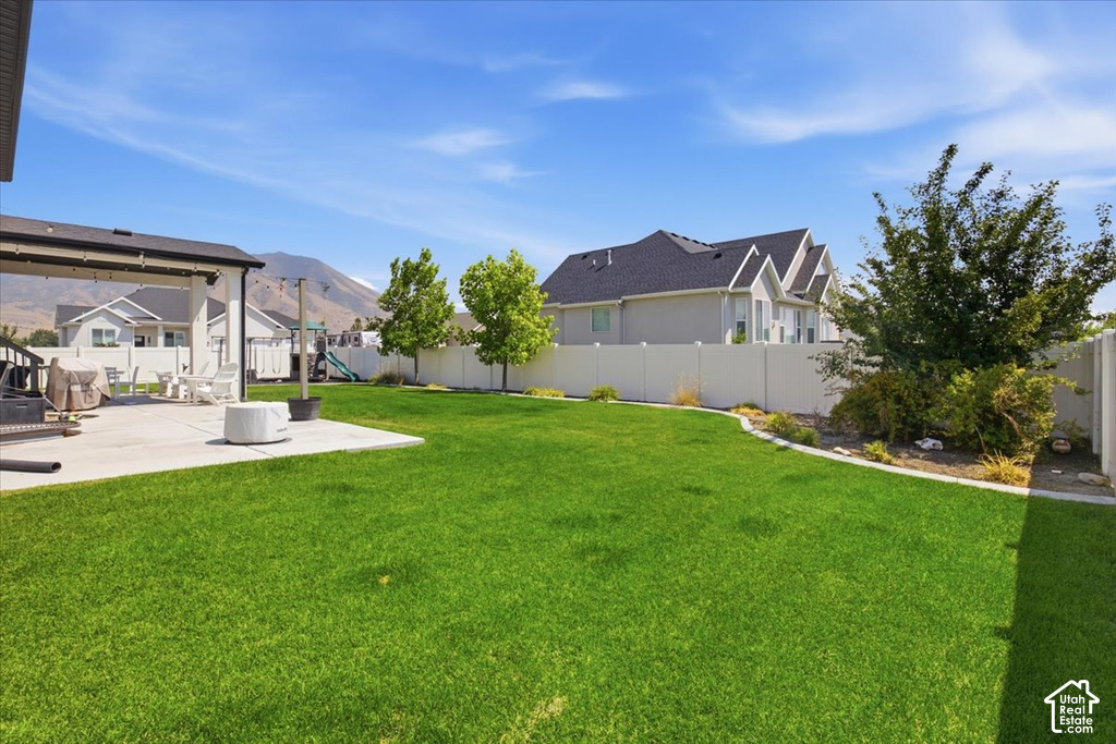 Expansive backyard featuring a meticulously manicured lawn, mature landscaping with established trees and shrubs, and mountain backdrop