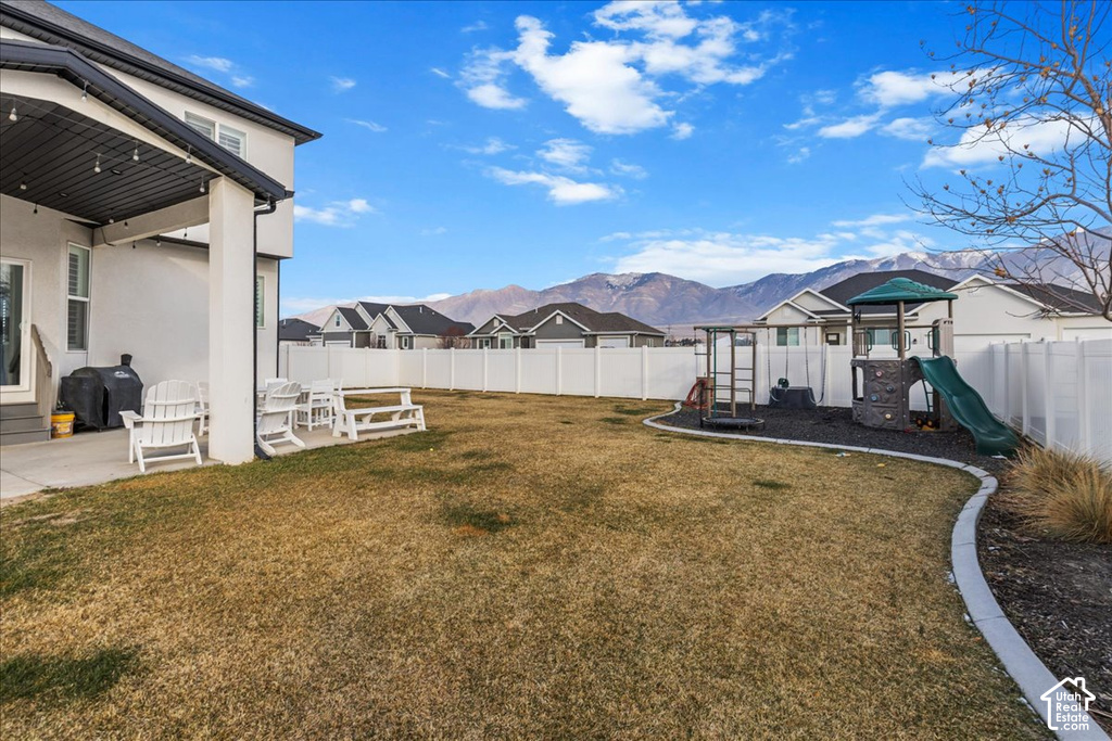 Expansive backyard featuring a covered patio, a manicured lawn, a white privacy fence, and a dedicated play area with a slide and climbing structure