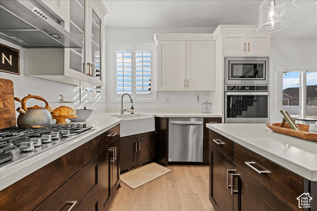 Gourmet kitchen featuring a gas range with stainless steel hood, built-in microwave and oven, apron front sink, and two-tone cabinetry with an island workspace