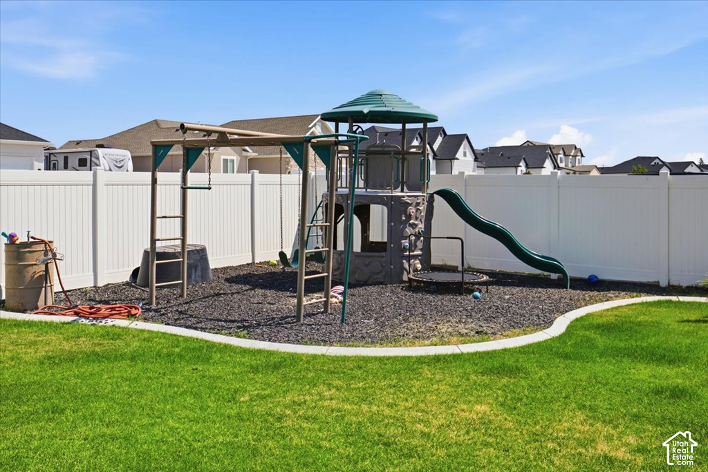 Expansive backyard featuring a manicured lawn, white privacy fencing, and a built-in play structure with a slide and swings