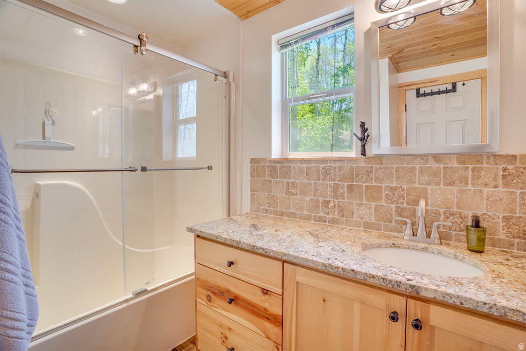 Bathroom featuring a wood-finish vanity with drawer storage, granite countertop, rectangular undermount sink, and tiled backsplash