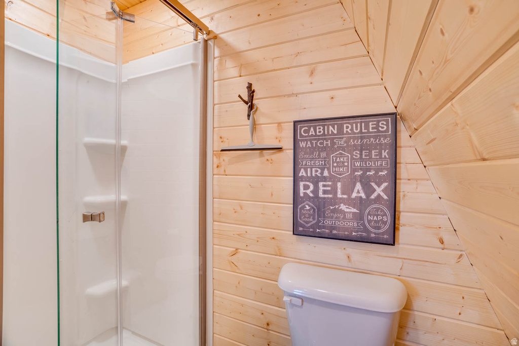 Three-piece bathroom featuring a shower enclosure with clear glass doors, white toilet, and natural wood paneling