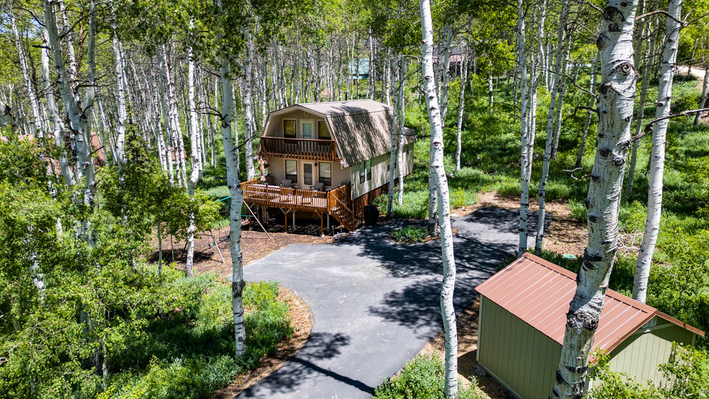 Cabin-style home featuring a rounded gambrel roof, upper-level balcony, and an extensive wood deck