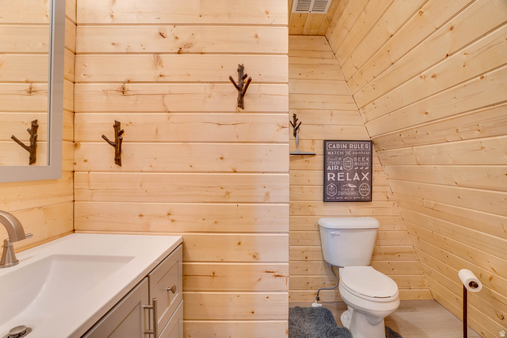 Bathroom featuring light wood paneling, a contemporary vanity with an integrated sink, brushed nickel faucet, and a toilet