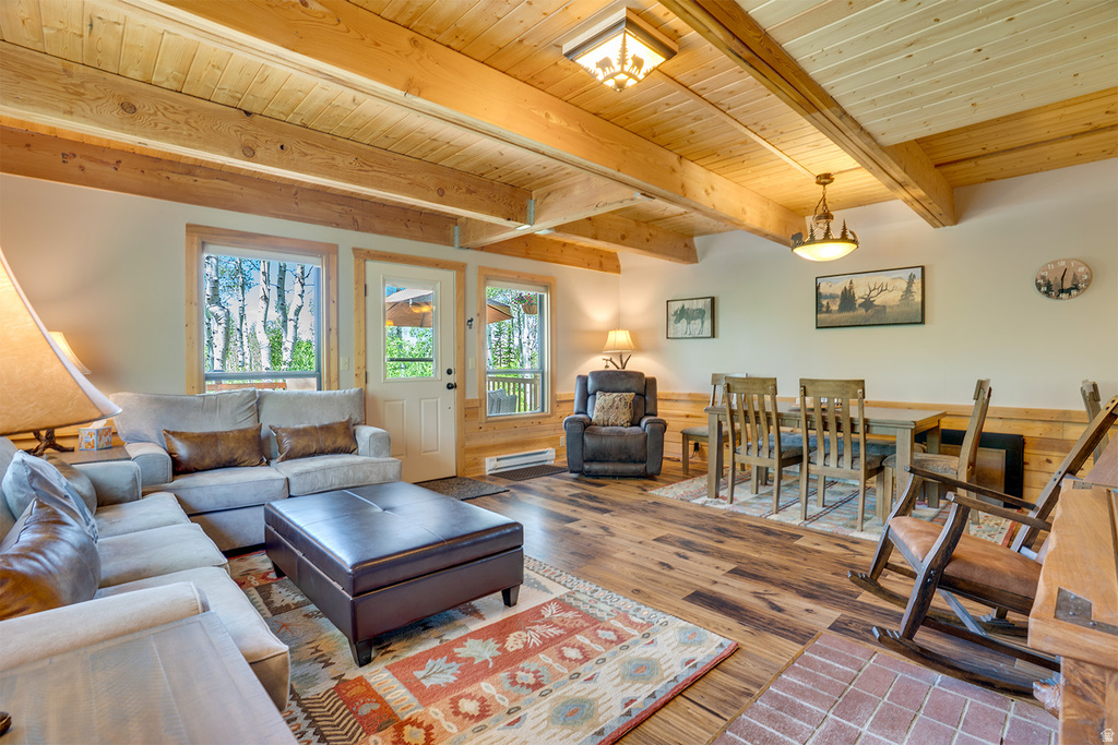 Open-concept living and dining area featuring wood-finish flooring, exposed wood beam ceiling, and a fireplace with a brick hearth