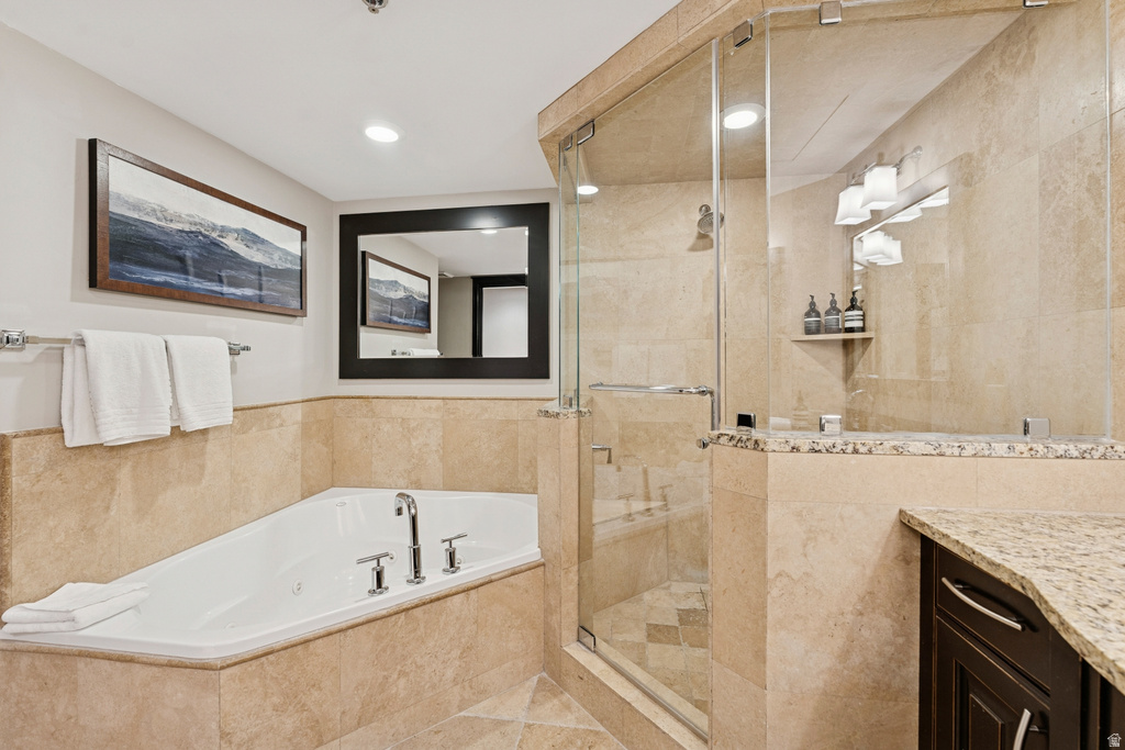 Bathroom featuring a built-in corner soaking tub with chrome fixtures, a glass-enclosed shower with a tiled surround, light-toned wall and floor tiling, a vanity with a granite countertop, and dark wood-finish cabinetry