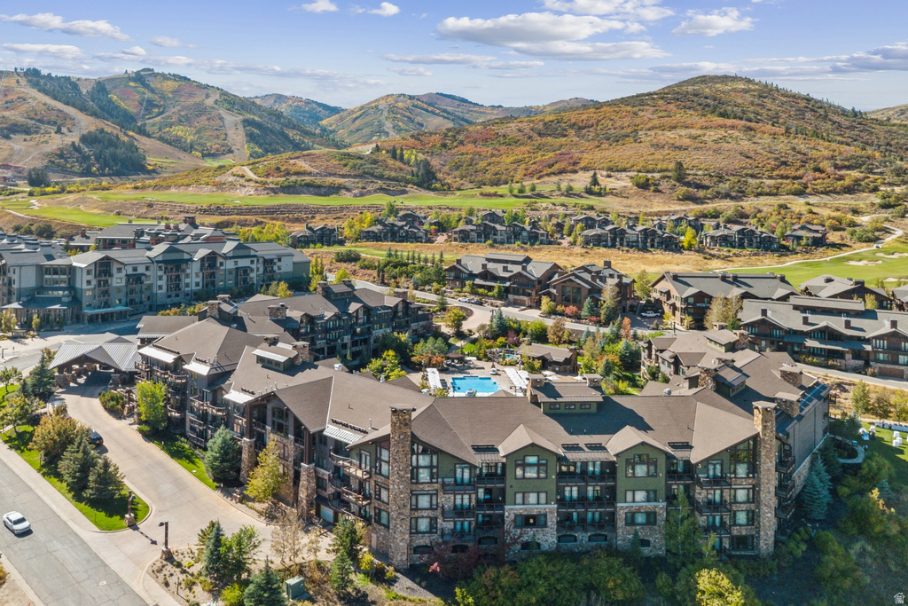 Multi-story residential complex featuring stone and wood-finish siding, a central outdoor swimming pool, individual balconies, a covered porte-cochère, and a surrounding landscape of hills and valleys