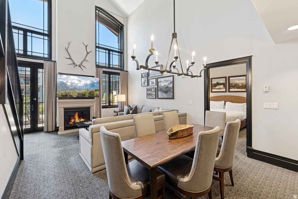Open-concept living space featuring a fireplace with a stone surround, a two-story vaulted ceiling, a large iron chandelier, black-framed windows, and a glass-paneled door leading to an outdoor area