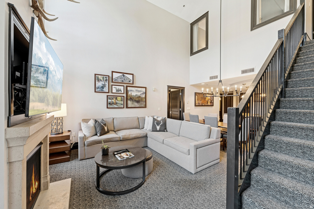 Spacious living area featuring a vaulted ceiling, a stone-finish fireplace, and an open staircase with dark wood-finish newel posts and railings