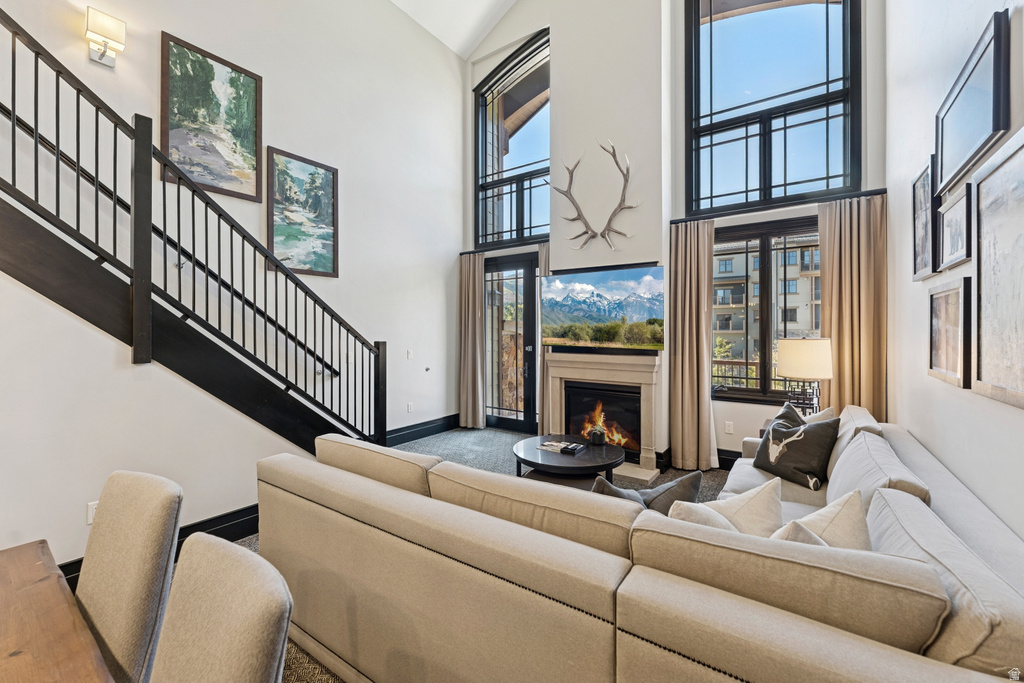 Two-story living area featuring a stone mantel fireplace, dark wood staircase with metal balusters, and expansive windows with dark framing
