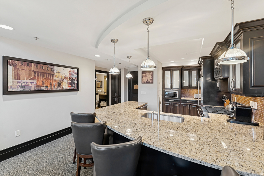Kitchen featuring a granite-topped island with an undermount sink, dark wood cabinetry, and a textured backsplash