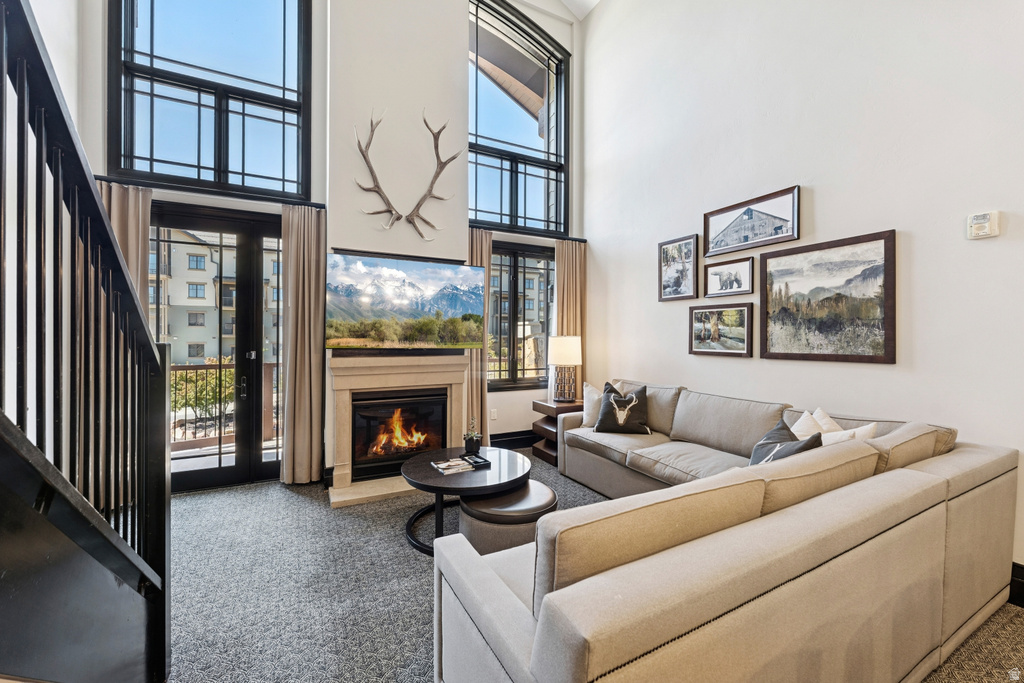 Living area featuring a floor-to-ceiling fireplace with a mantel, a wall-mounted flat-screen display, and a two-story window system with transoms