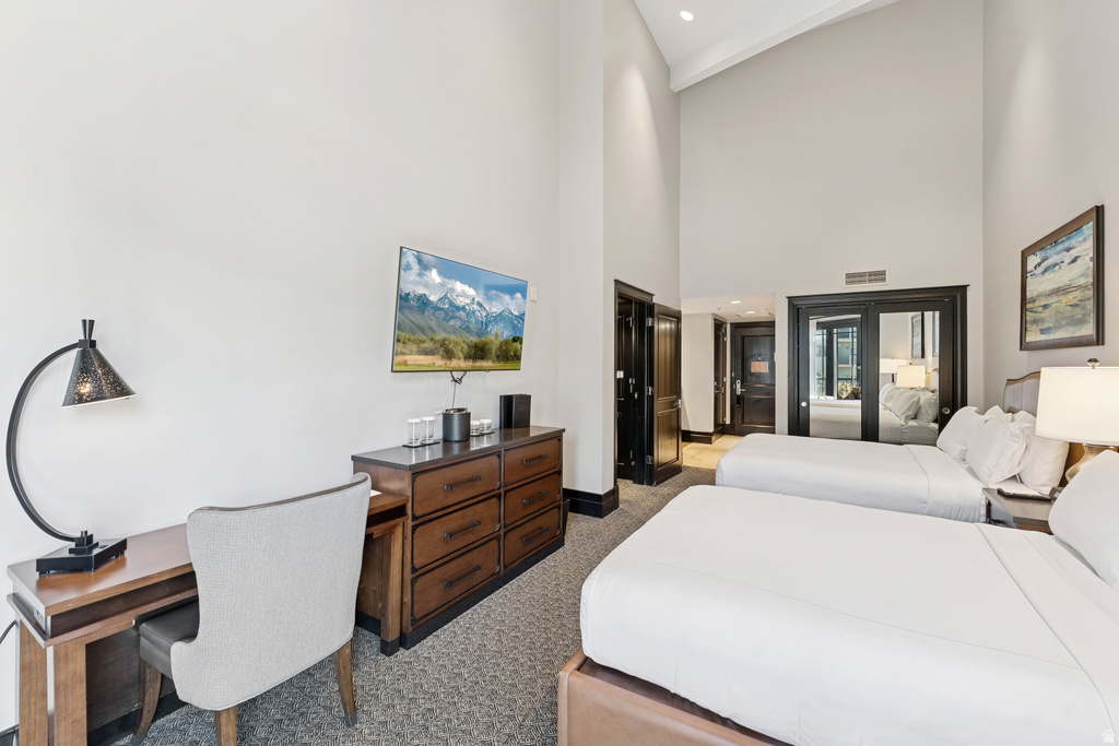 Spacious room featuring vaulted ceilings, a built-in wooden desk, a dark wood dresser, a wall-mounted television, and two beds