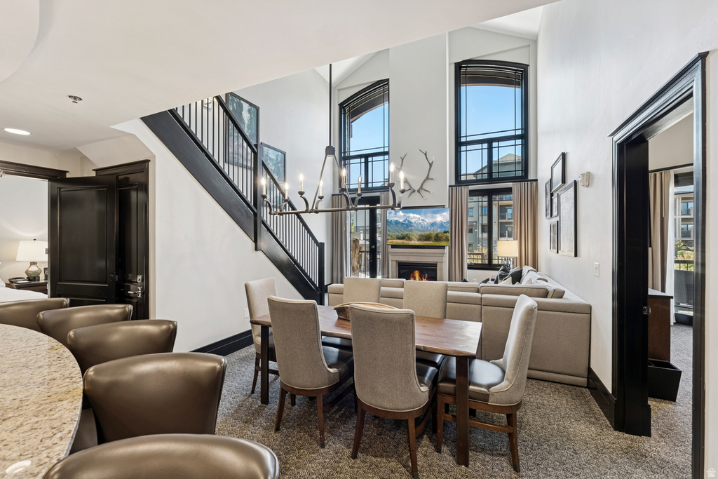 Dining area featuring a wood-finish table, a linear chandelier, and access to a living area with a fireplace