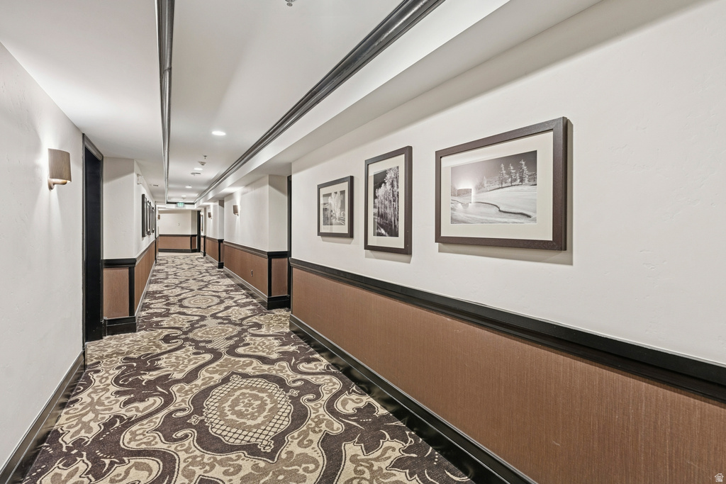 Hallway featuring patterned carpet, wainscoting with decorative trim, recessed lighting, and wall sconces