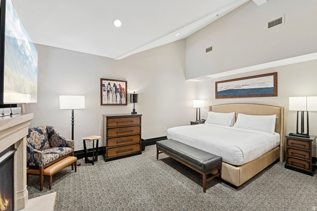 Vaulted ceiling bedroom featuring a neutral color palette, built-in fireplace with stone-finish mantel, carpeted flooring, and dark wood-finish furnishings