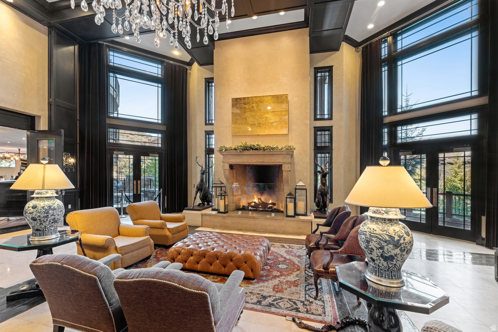 Grand living space featuring a two-story stone fireplace with mantel, polished marble flooring, a tiered crystal chandelier, and expansive windows with black trim and transoms