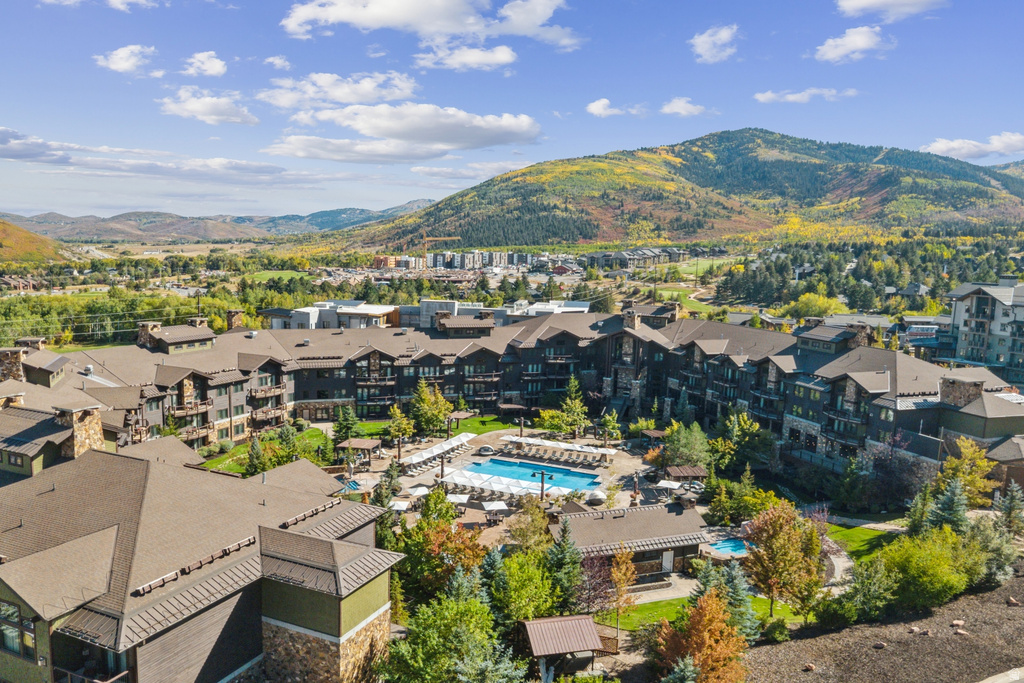 Expansive property featuring multiple buildings with dark siding and stone accents, a large outdoor swimming pool, and a smaller separate pool