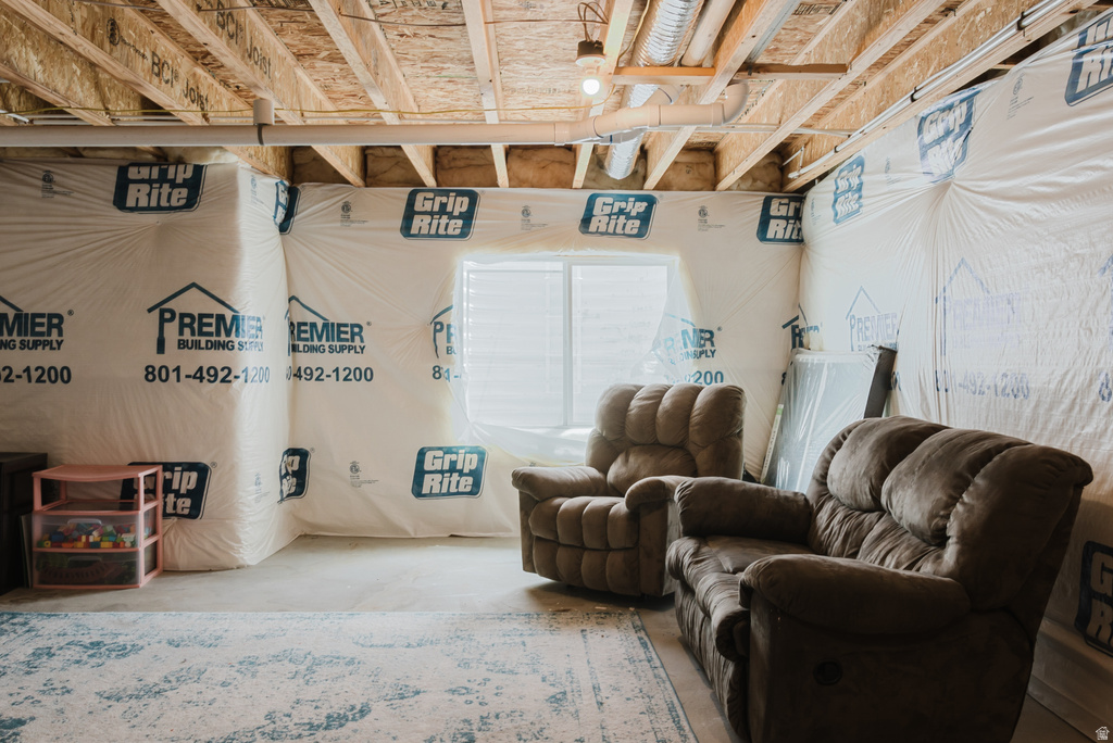 Unfinished basement space featuring exposed wood joists and subflooring, insulated walls, a single window with blinds, and concrete flooring