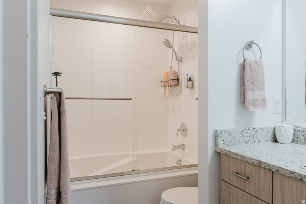 Bathroom featuring a combination bathtub and shower with sliding glass doors, a vanity with granite-finish countertop, and wood-finish cabinetry