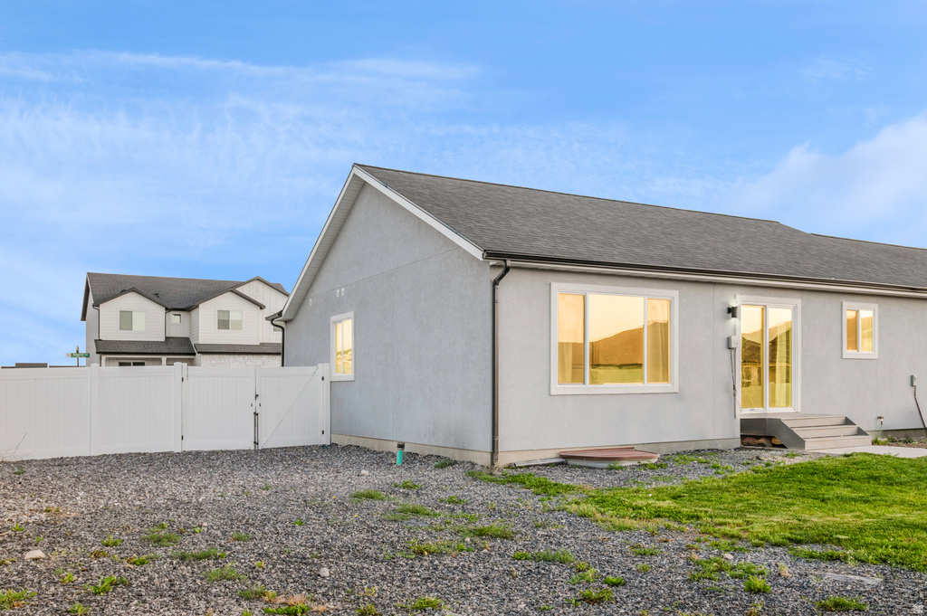 Rear exterior featuring a gray stucco finish and a dark shingle roof