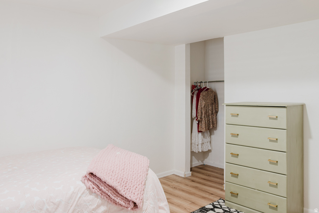 White walls with a recessed ceiling feature, light wood-finish flooring, and an open closet space with a clothing rod