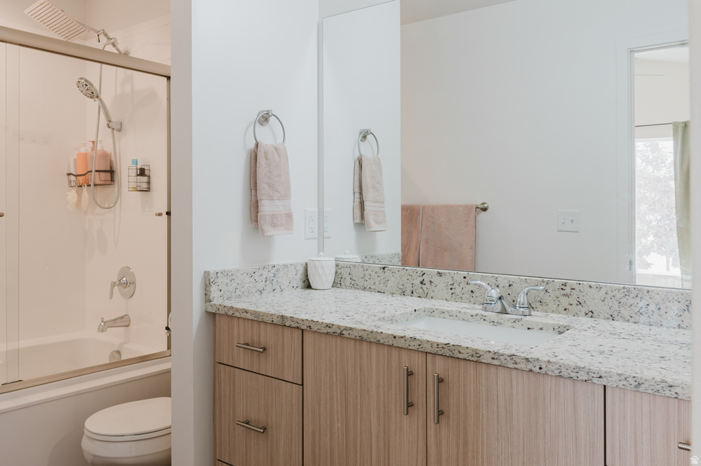 Bathroom featuring a light-toned wood-finish vanity with drawer and cabinet storage, a speckled countertop with an integrated sink, a large mirror, and a tub with a shower head and sliding glass enclosure