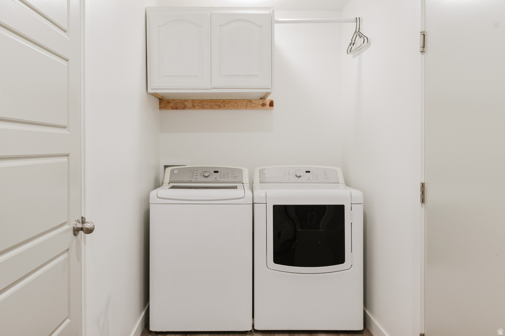 Dedicated laundry area featuring white shaker-style cabinetry, wood-finish flooring, white walls, and a built-in hanging rod