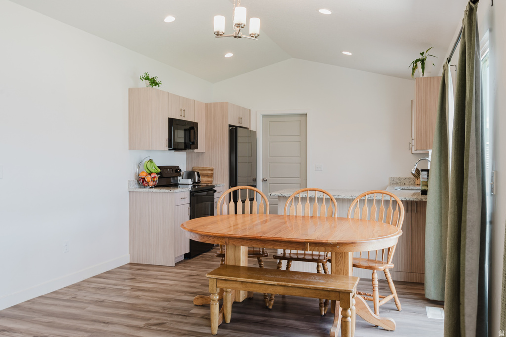 Open-concept kitchen and dining area featuring vaulted ceilings, recessed lighting, and wood-finish flooring
