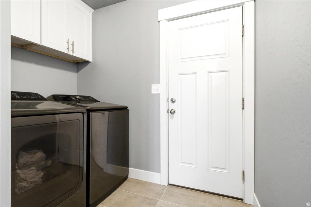 Laundry area featuring white cabinetry, modern front-loading appliances, light gray walls, white trim, and neutral tile flooring