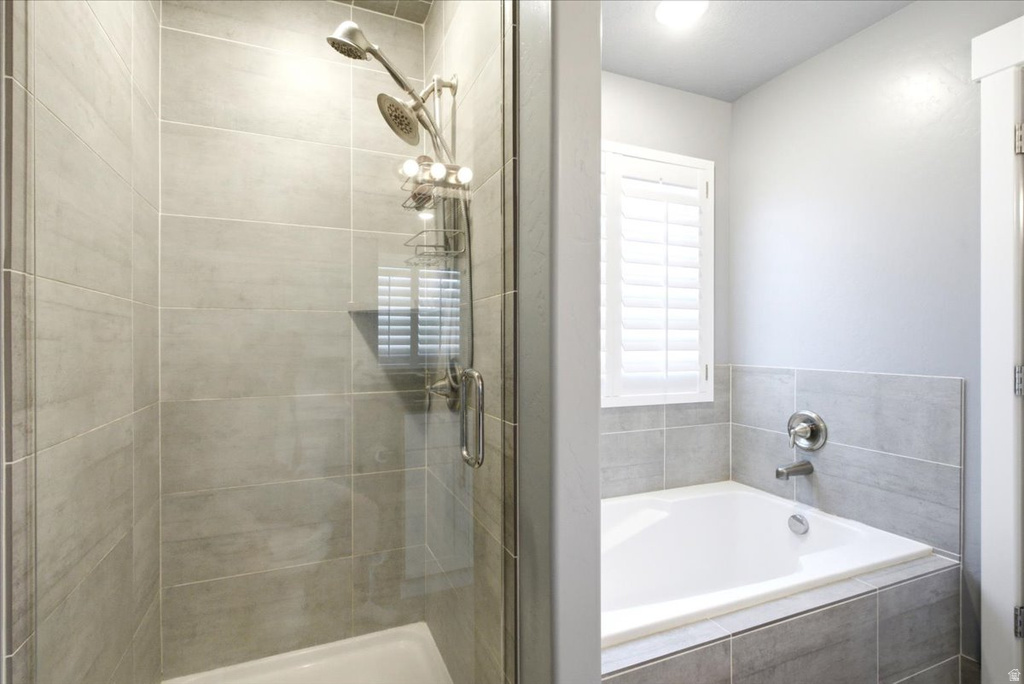 Bathroom featuring a tiled shower enclosure with glass door, a dual-head shower system, and a built-in bathtub with tiled surround and window with plantation shutters
