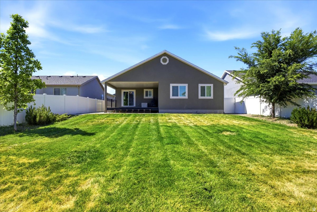 Spacious backyard featuring a large green lawn, covered patio with sliding glass door, and privacy fencing