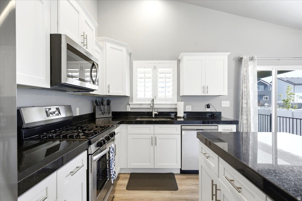 Modern kitchen featuring white cabinetry, dark countertops, stainless steel appliances, and wood-finish flooring