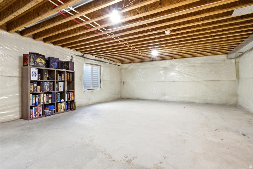 Unfinished basement featuring exposed wood ceiling joists, concrete flooring, and a small basement window with horizontal slats
