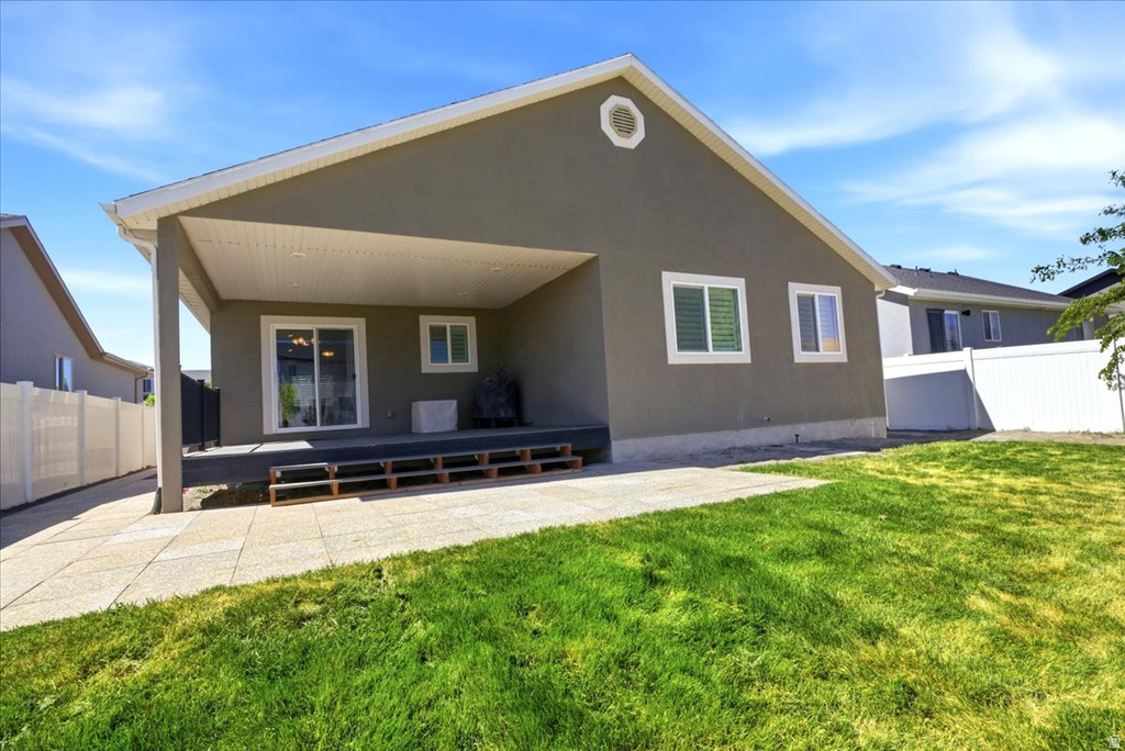 Rear exterior featuring a covered patio, a sliding glass door, a paved patio area, a green lawn, and privacy fencing